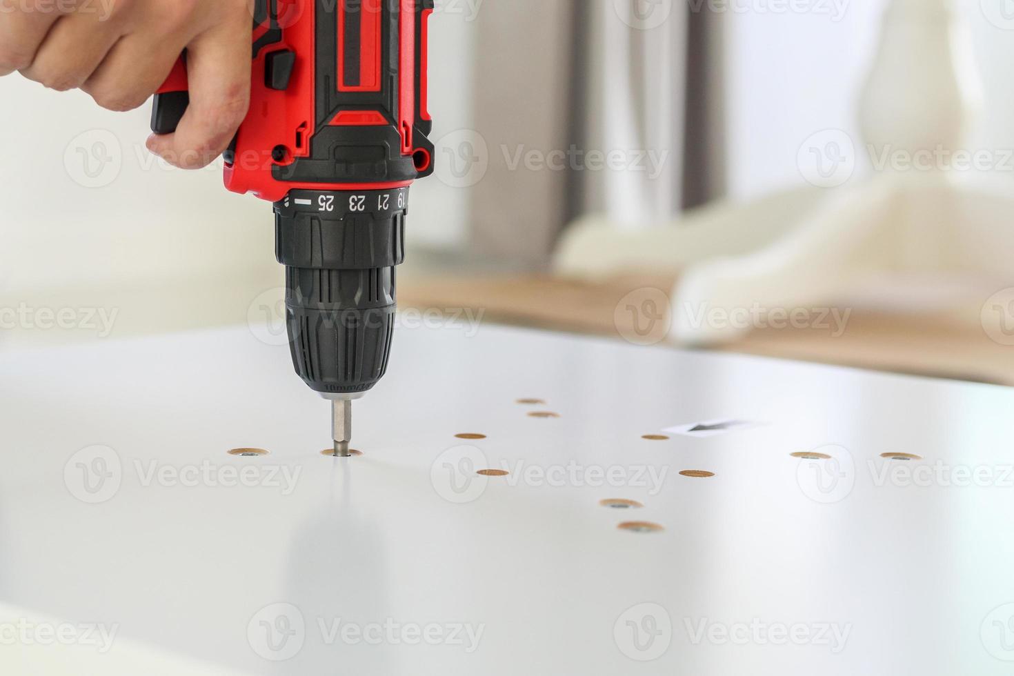 hombre montando muebles de mesa blancos en casa usando un destornillador inalámbrico foto