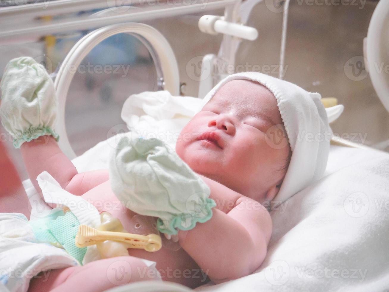 Newborn baby girl inside incubator in hospital post delivery room photo