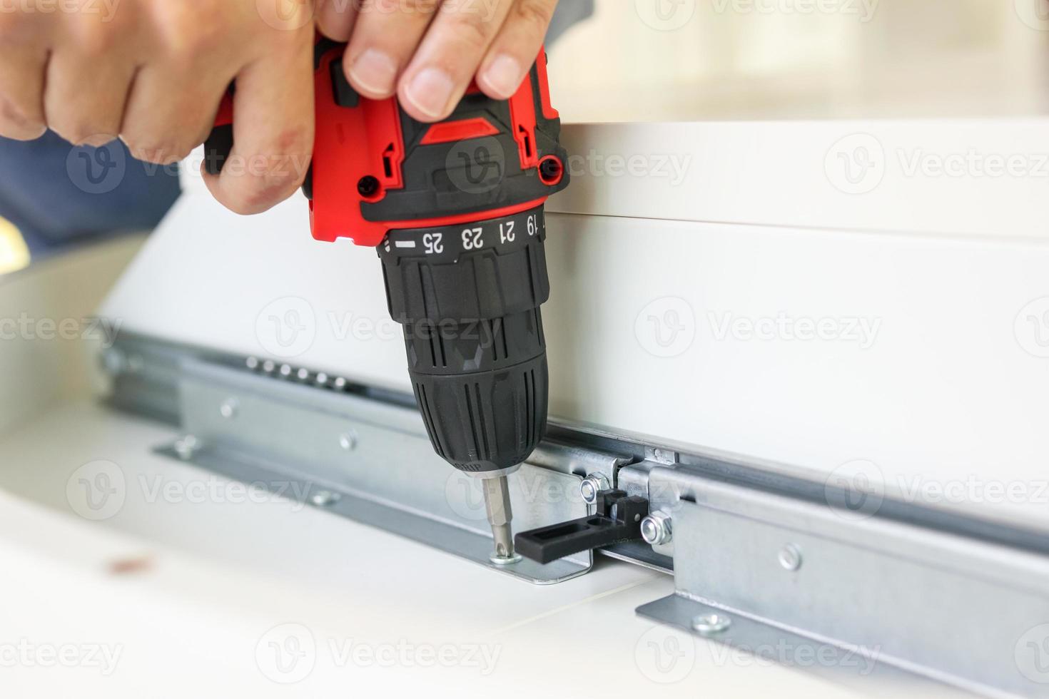 man assembling white table furniture at home using cordless screwdriver photo