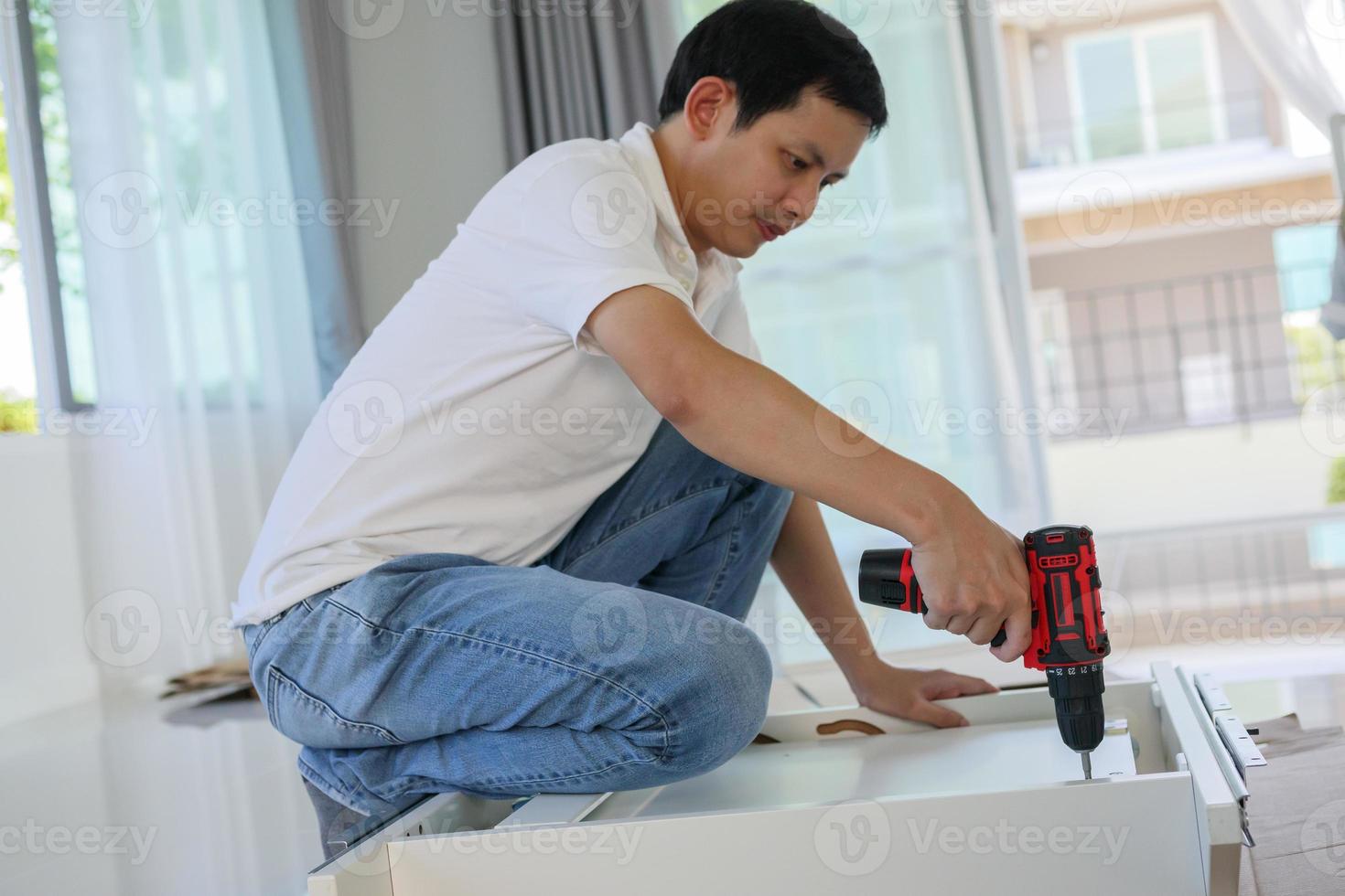 Asian man assembling white table furniture at home using cordless screwdriver photo