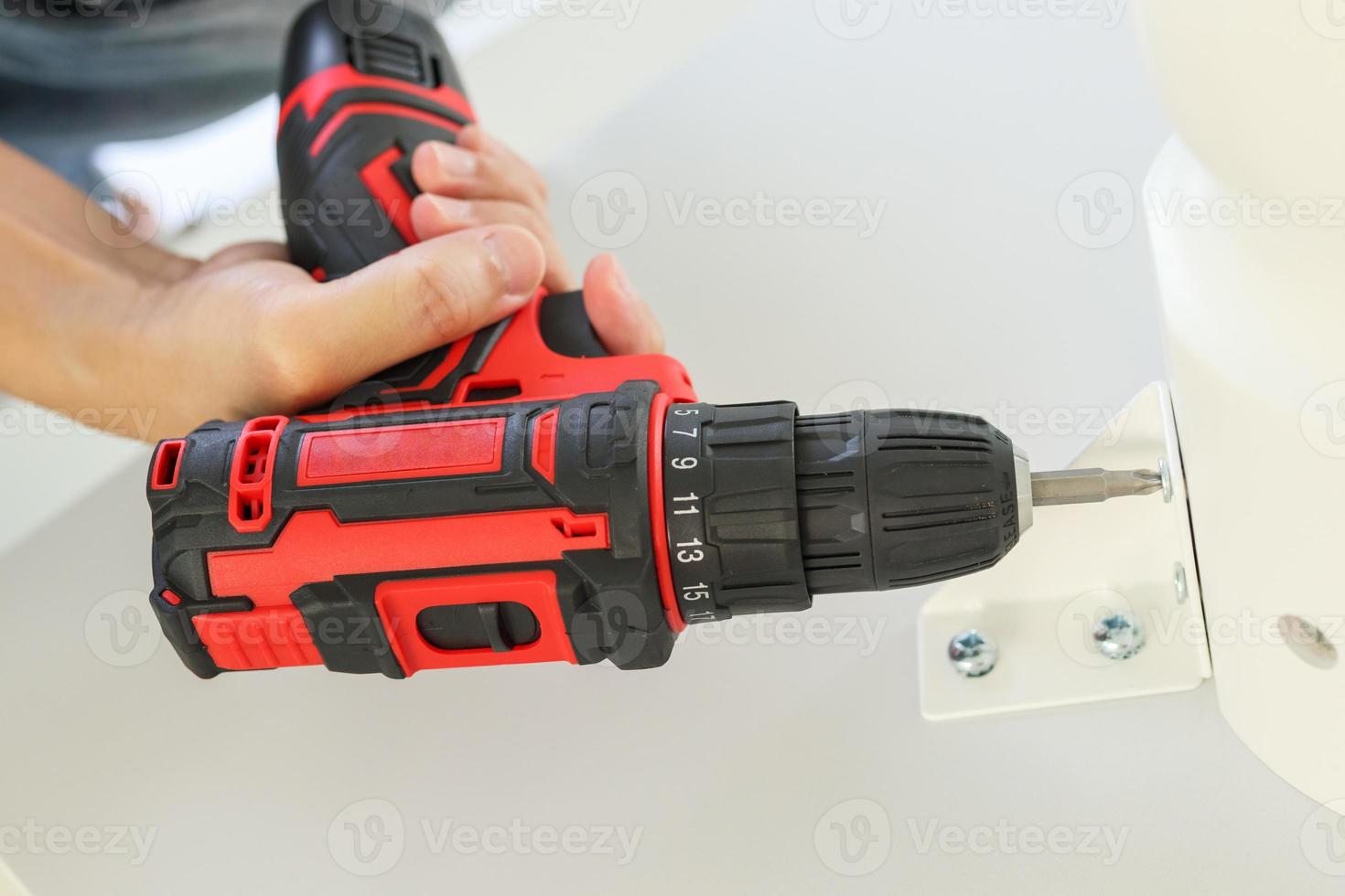 hombre montando muebles de mesa blancos en casa usando un destornillador inalámbrico foto