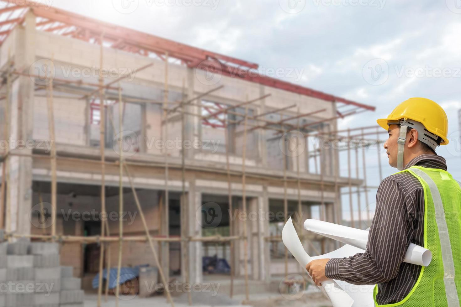 young professional engineer in protective helmet and blueprints paper at the house building construction site photo