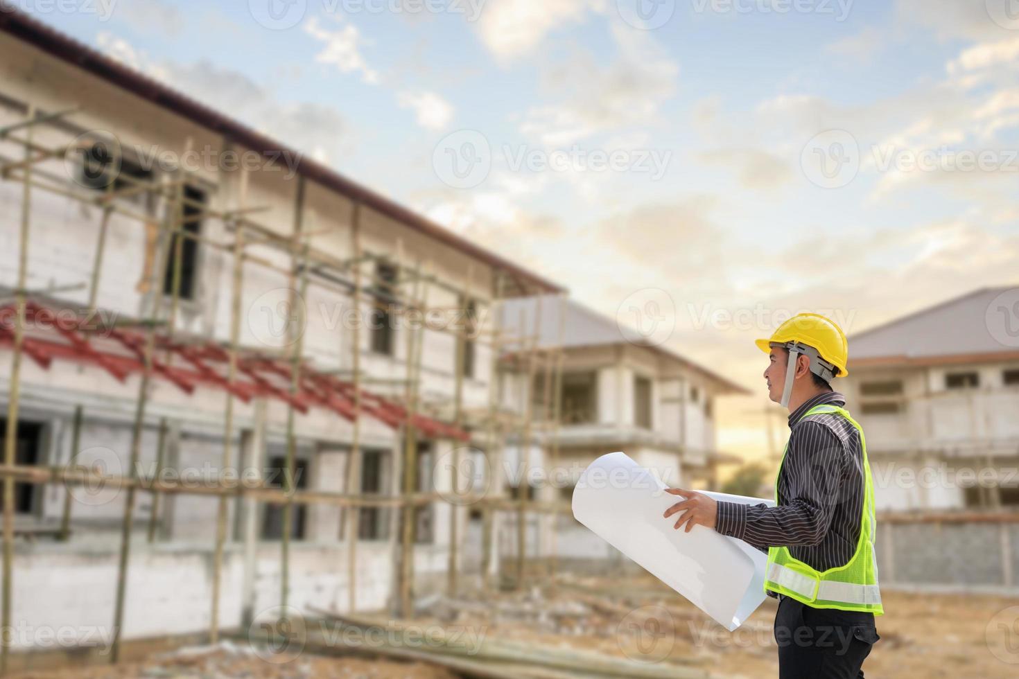 joven ingeniero profesional en casco protector y papel de planos en el sitio de construcción de la casa foto