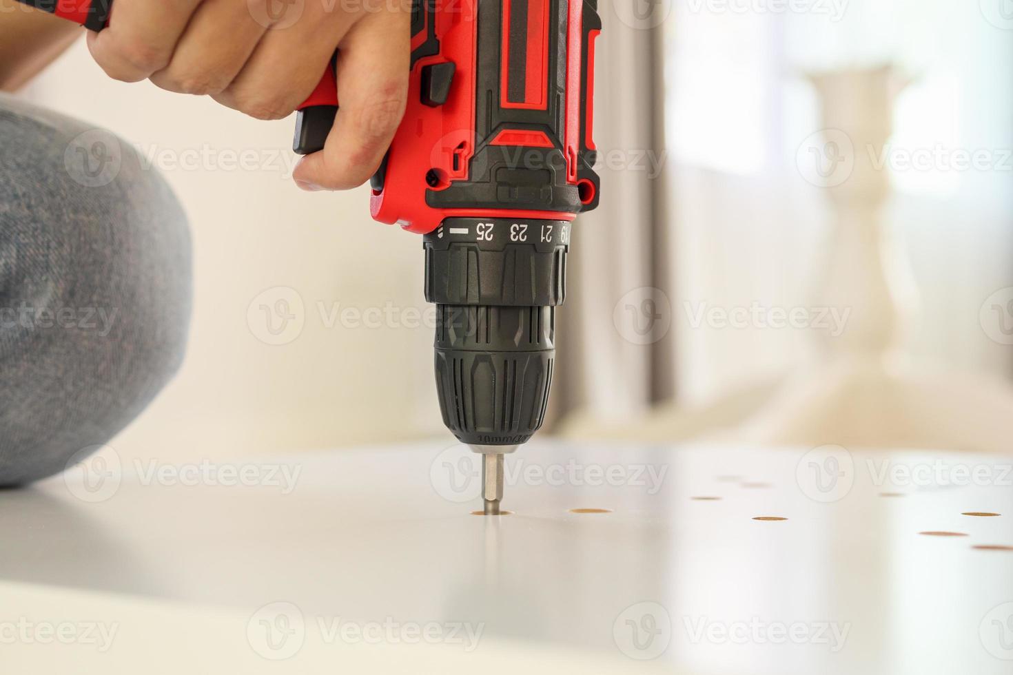 hombre montando muebles de mesa blancos en casa usando un destornillador inalámbrico foto