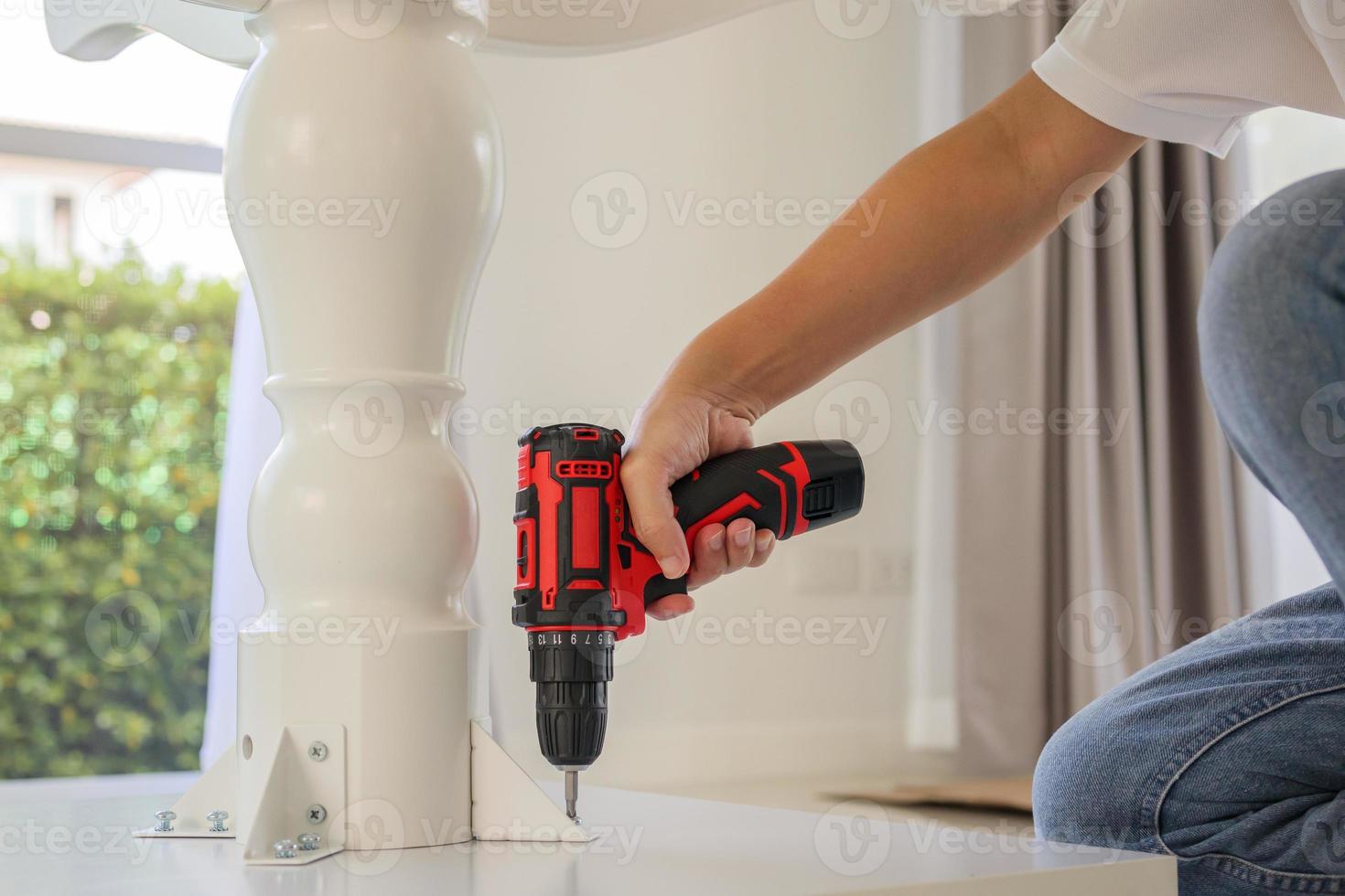 man assembling white table furniture at home using cordless screwdriver photo