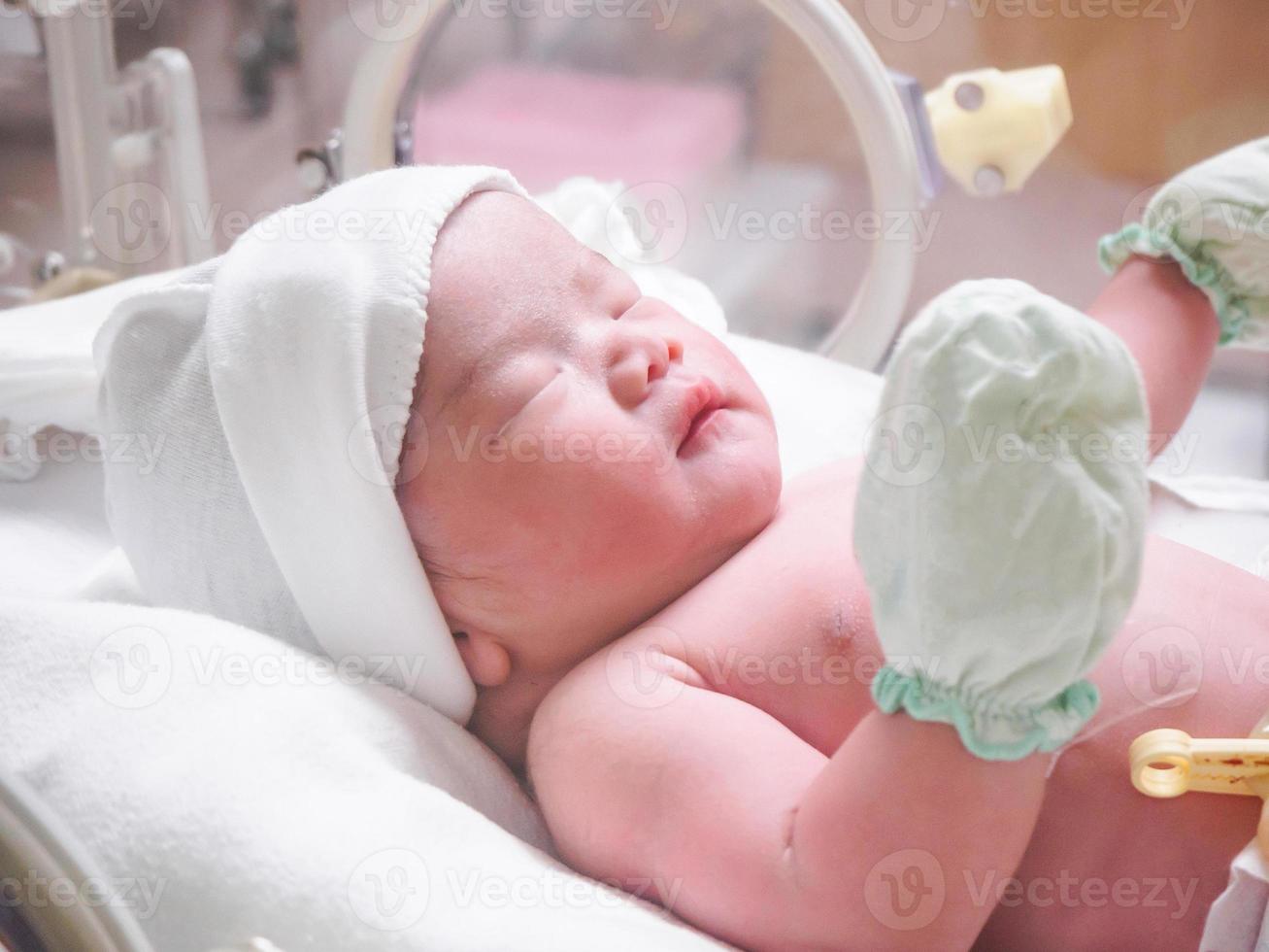 Newborn baby girl inside incubator in hospital post delivery room photo