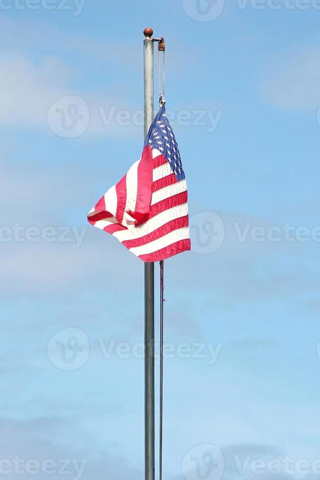 An old American flag on the tip of the flag with a torn in the wind on the flagpole against a blue sky background. photo