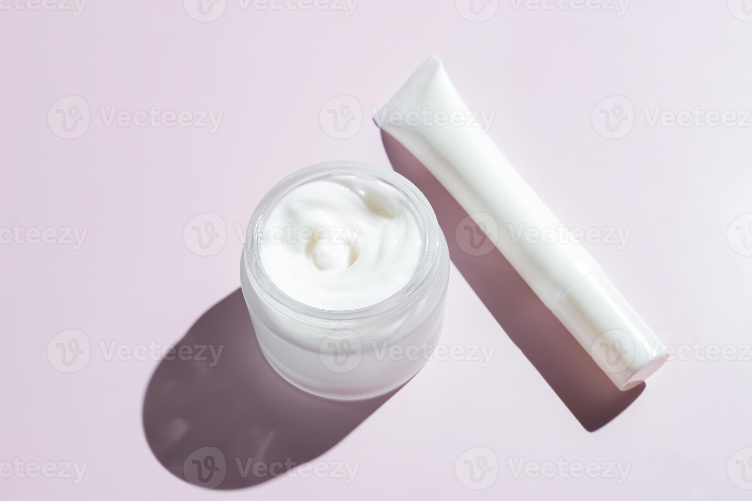 Face and eye cream in white unbranded packaging on pink background with