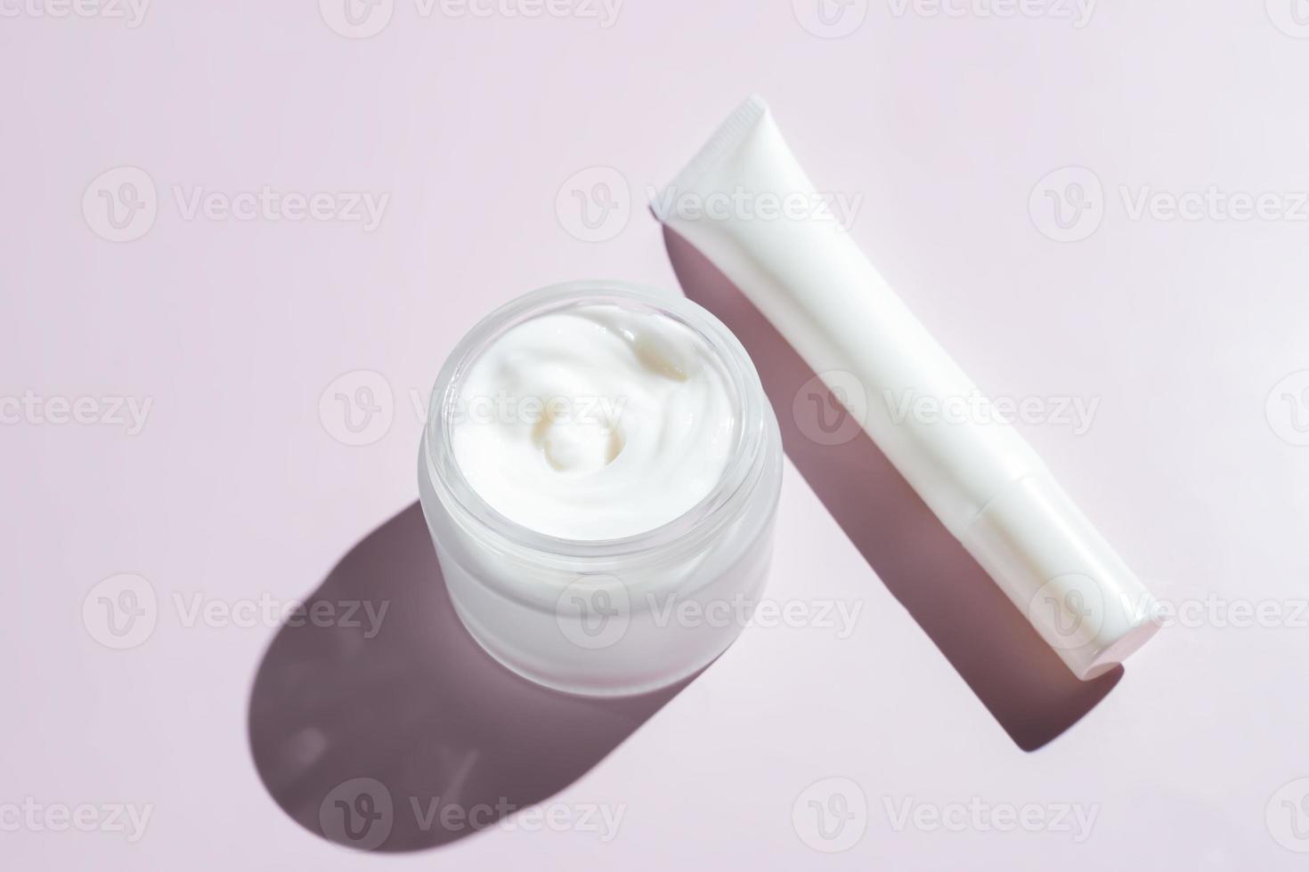 Face and eye cream in white unbranded packaging on pink background with harsh shadows. Skin care daily products for healthy and fresh skin. Packaging design photo