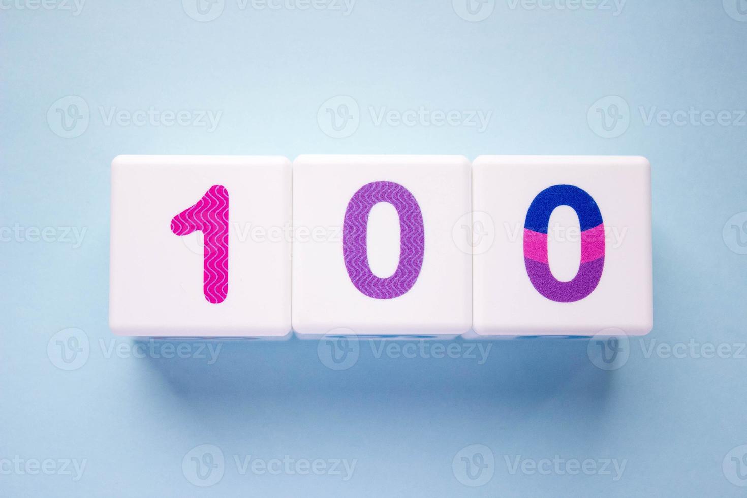 Close-up photo of a white plastic cubes with a colorful number 100 on a blue background. Object in the center of the photo