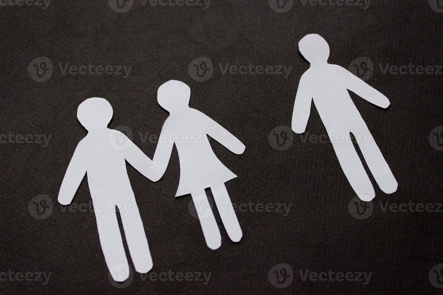 Silhouettes of people cut from paper. Couple holding hands and next to a lonely man on black background. The concept of relationships, love, jealousy, loneliness, treason photo