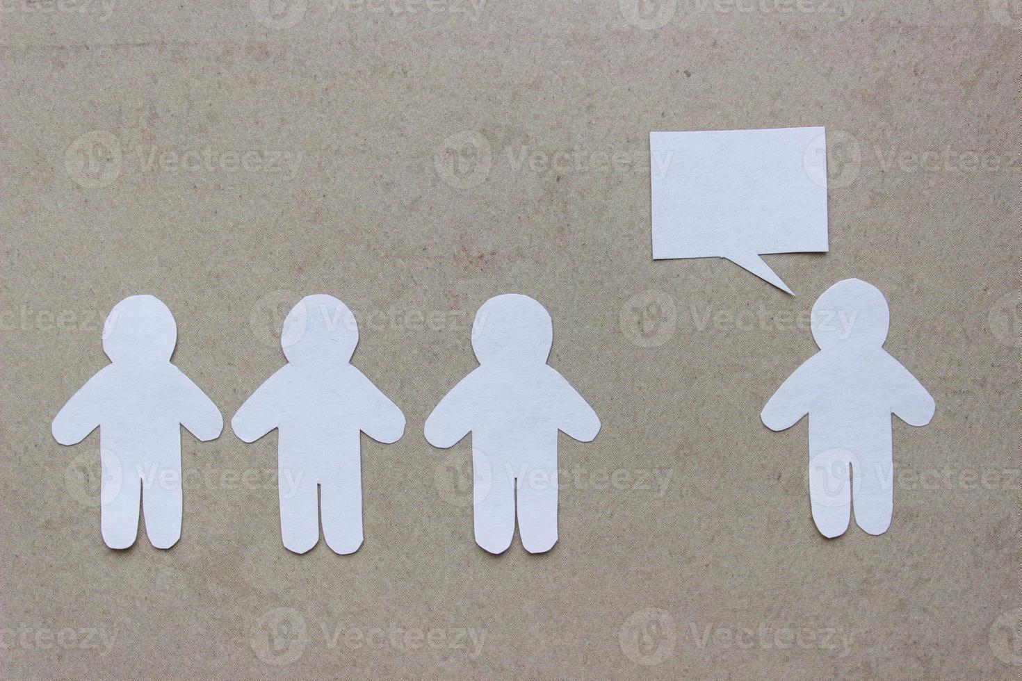 Silhouettes of people cut from white paper on a beige background. A group of people stands in front of one person who is speaking speech-bubble. Communication, leadership, teamwork concept photo