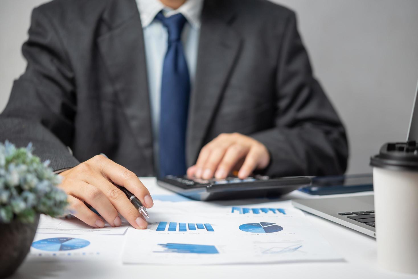 Businessman hand pointing paperwork chart report analysis statistic and document financial graph with computer laptop at office.Business investment marketing on desk in company. photo