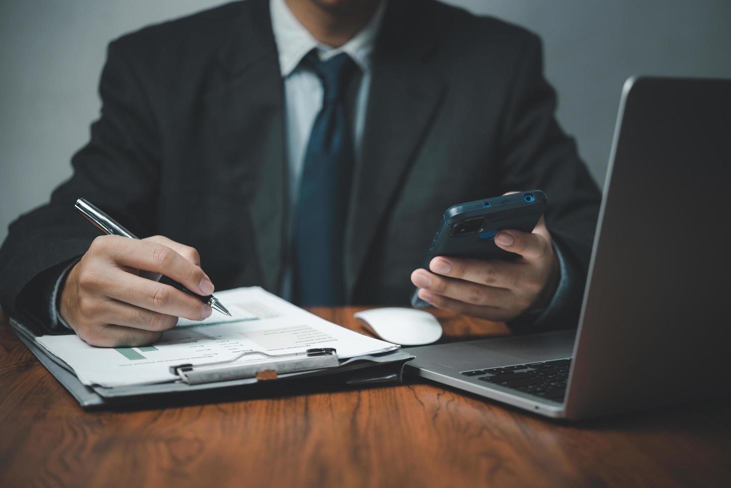 mano de hombre de negocios que sostiene el teléfono móvil y la pluma con gráficos y gráficos documentos de negocios en el escritorio. inversión y análisis económico. concepto de negocio financiero y fiscal. foto