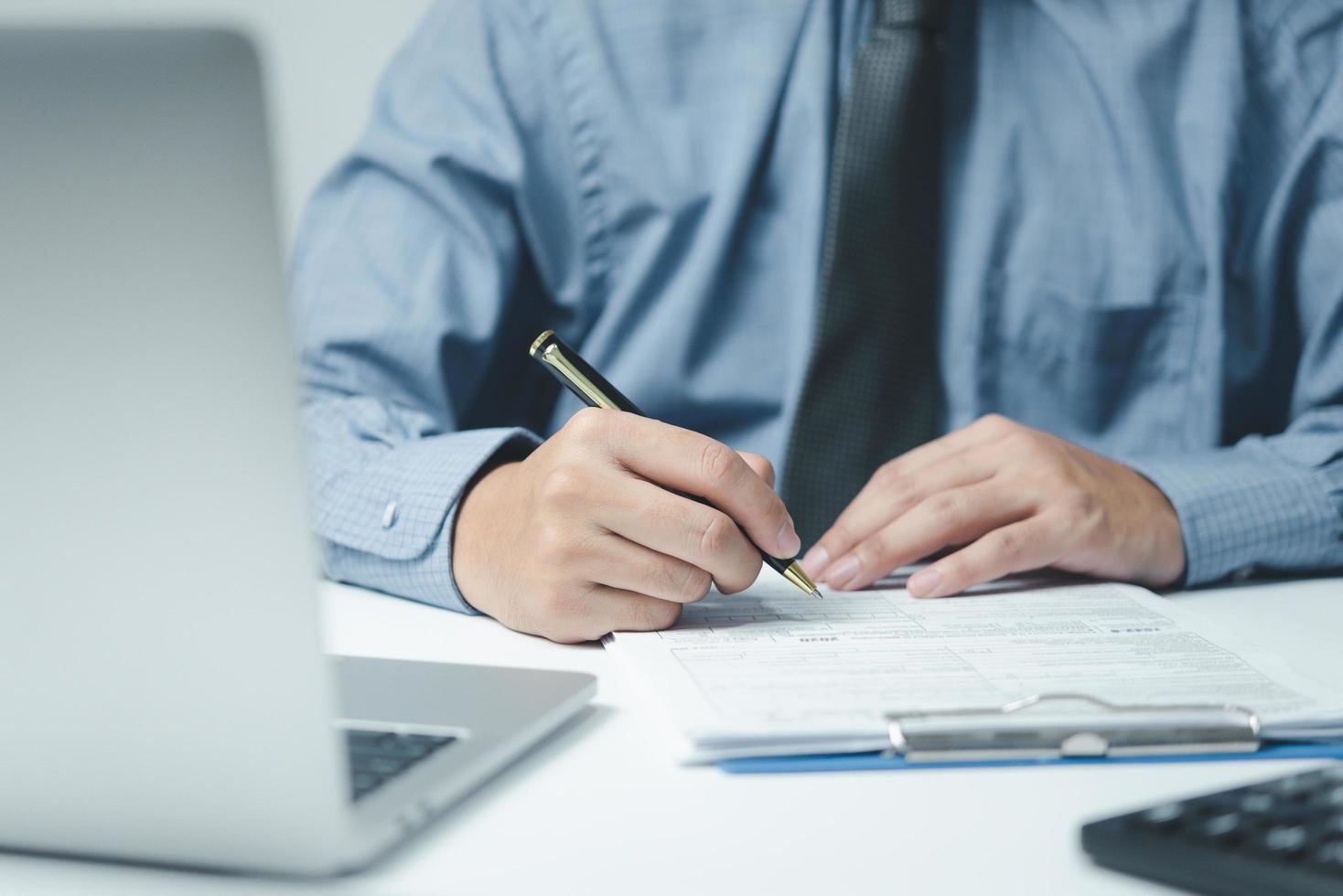 mano que sostiene la pluma que escribe papeleo documento comercial inversión financiera o contrato de firma trabajo y seguro en el escritorio. foto