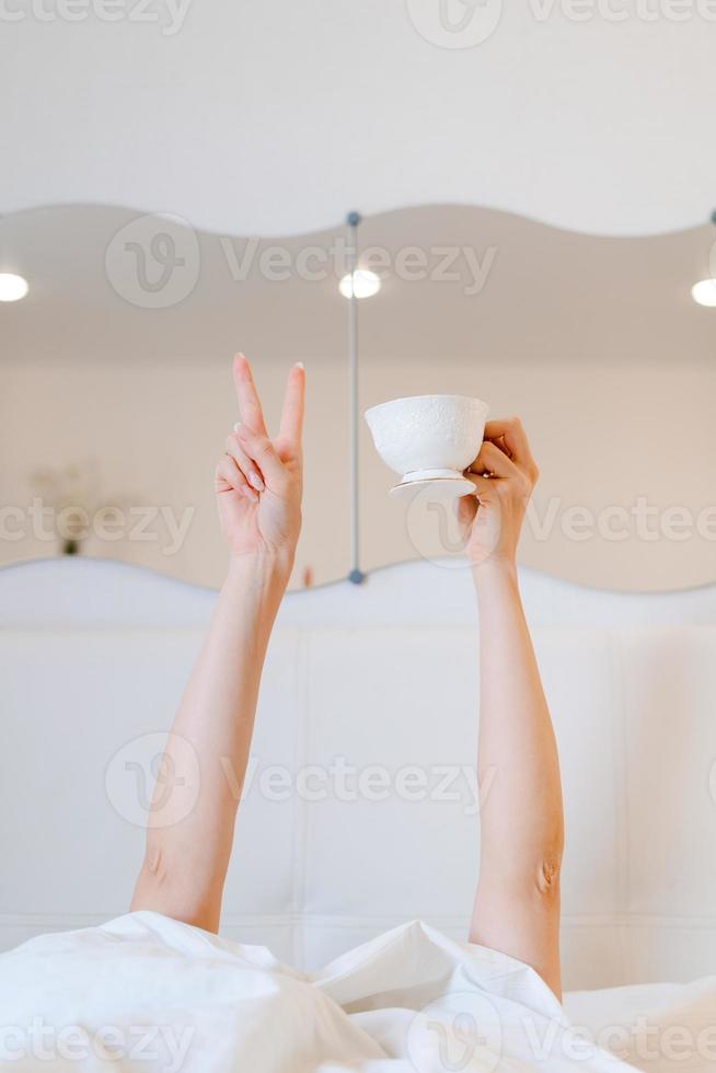 Young woman with a coffee mug in bed with white linens. Minimal happy morning photo