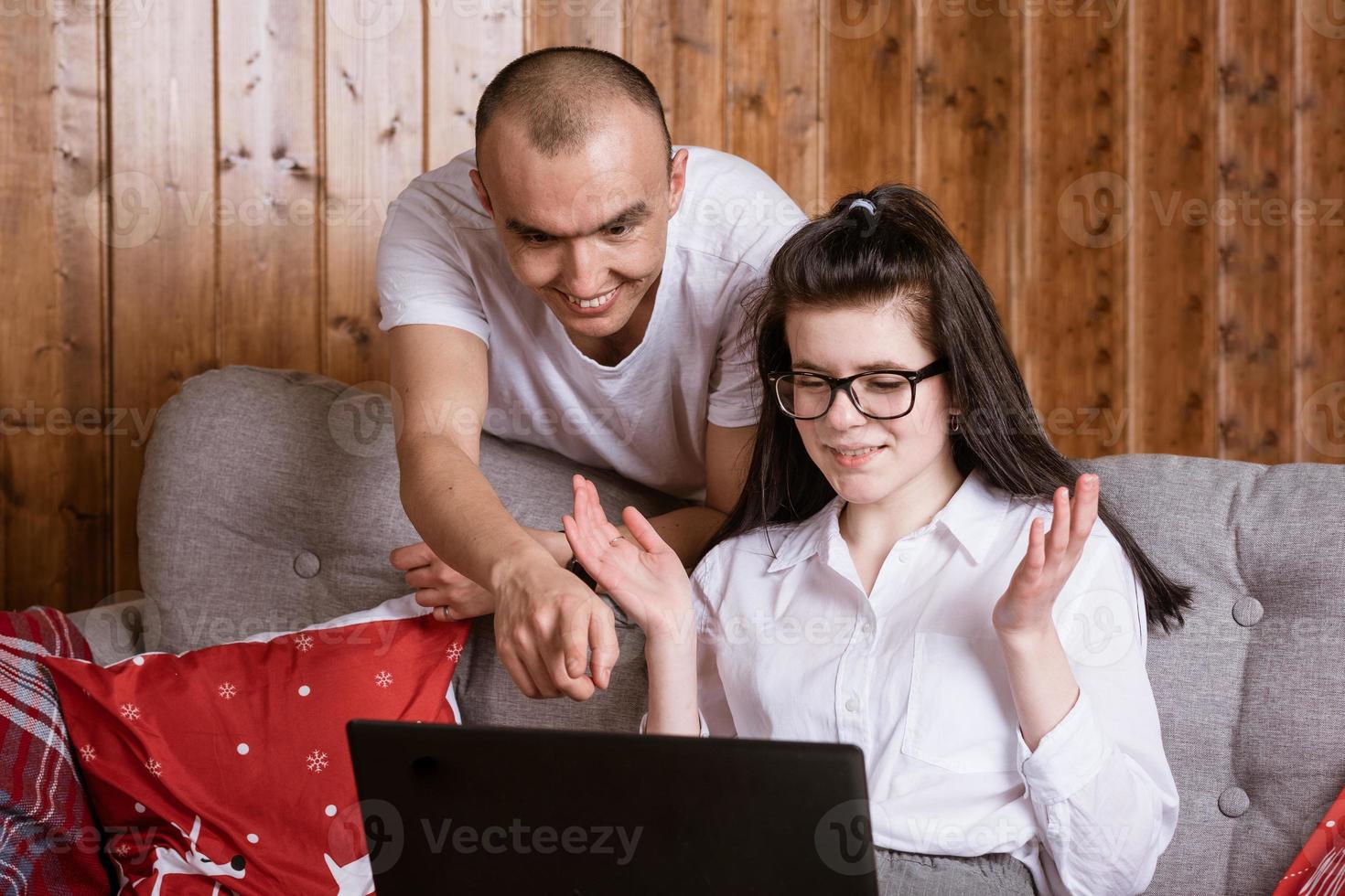 A young couple at home sitting on the couch communicating online via laptop with relatives photo