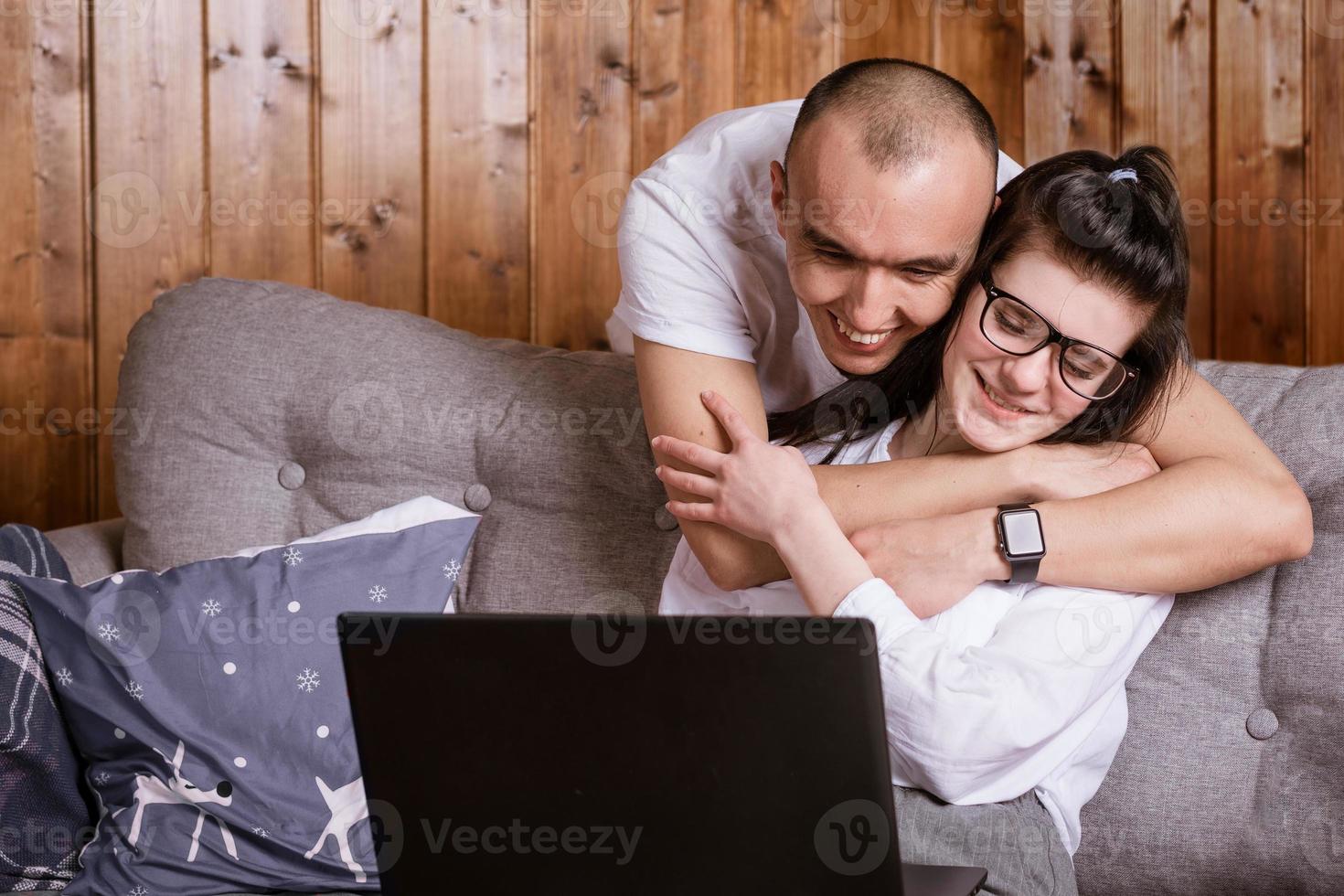 A young couple at home sitting on the couch communicating online via laptop with relatives photo