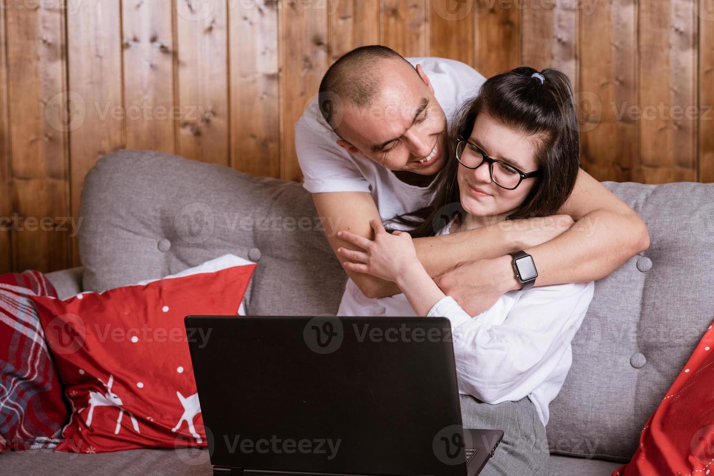 A young couple at home sitting on the couch communicating online via laptop with relatives photo