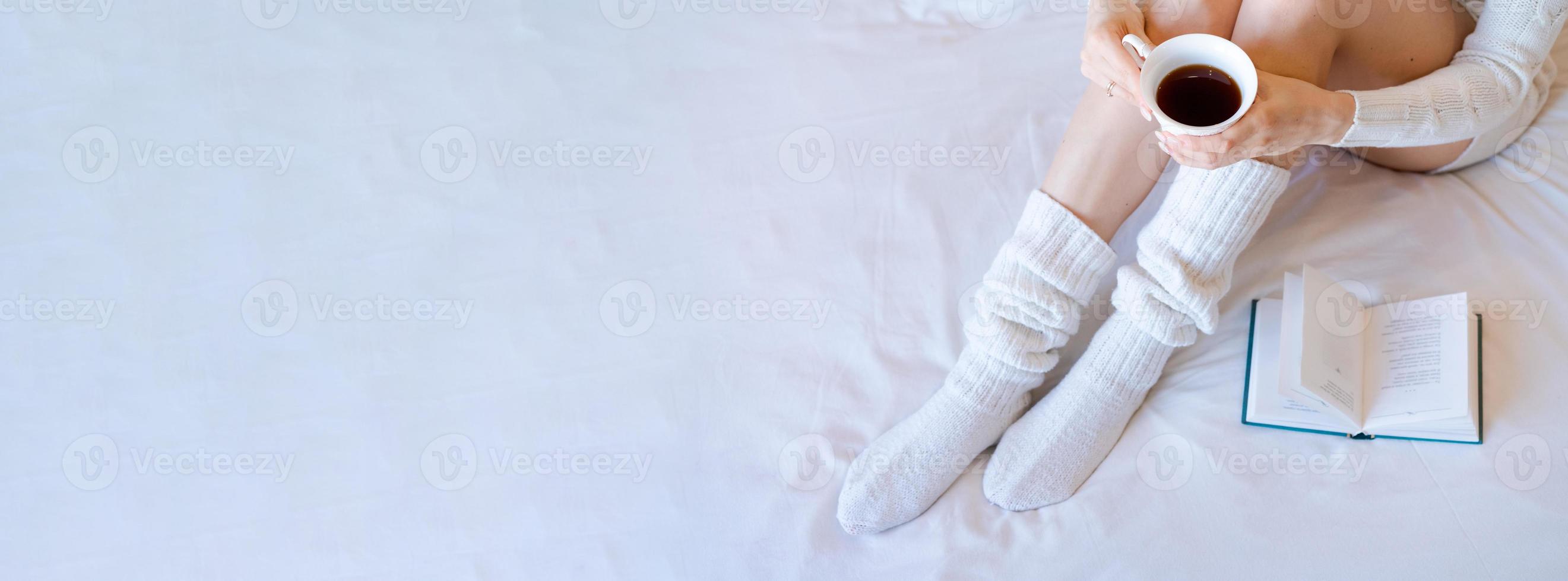 Lazy time in bed. Young woman in knitted knee socks on a white sheet reading photo