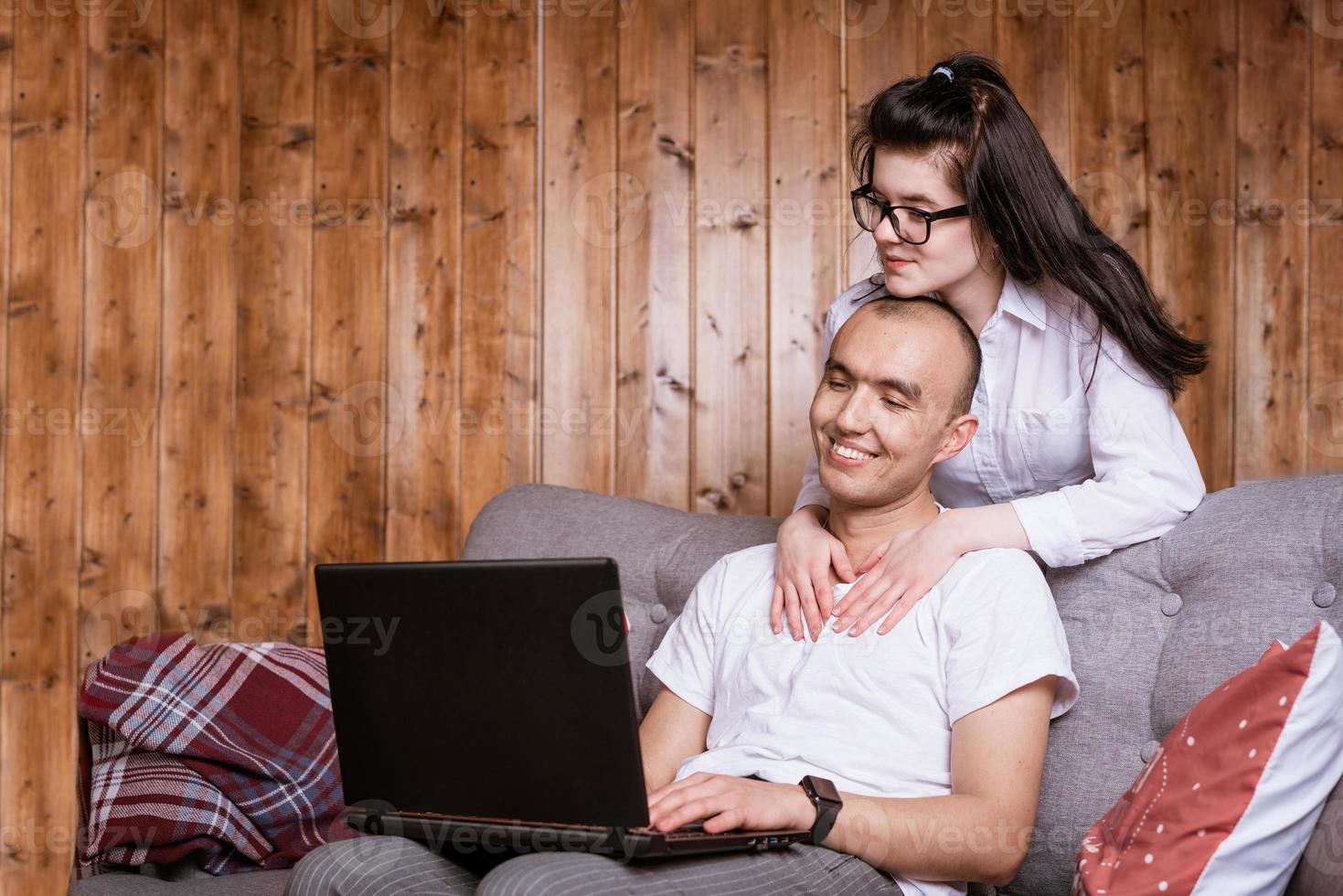 A young couple at home sitting on the couch communicating online via laptop with relatives photo