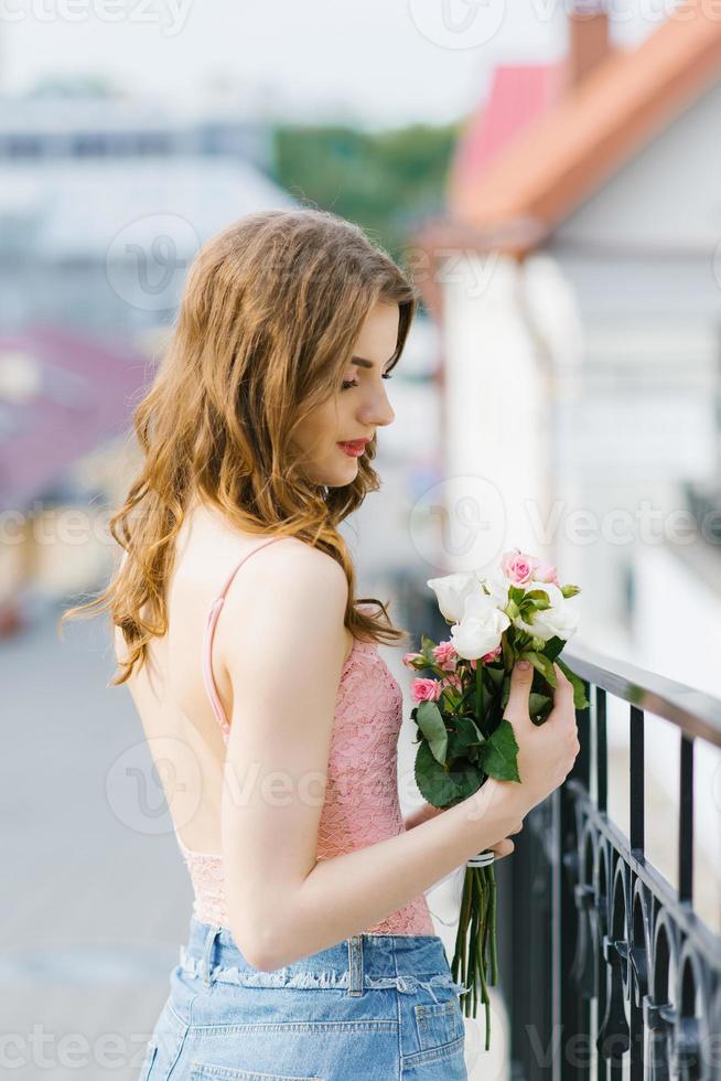 una hermosa joven con ropa ligera sostiene un ramo de rosas en sus manos foto