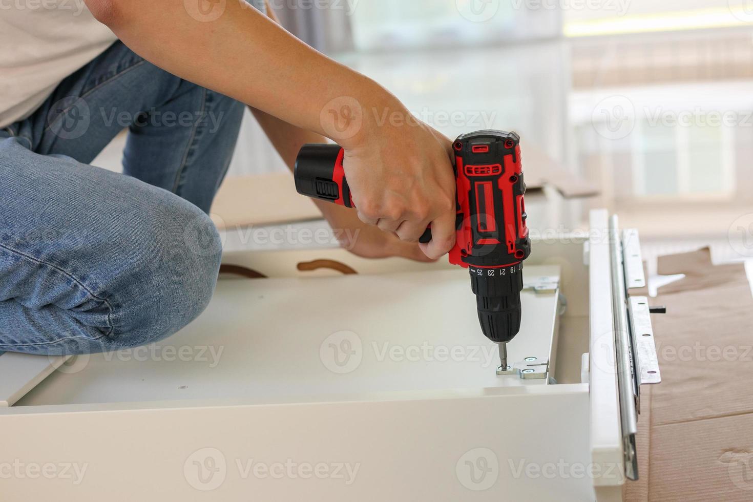 man assembling white table furniture at home using cordless screwdriver photo