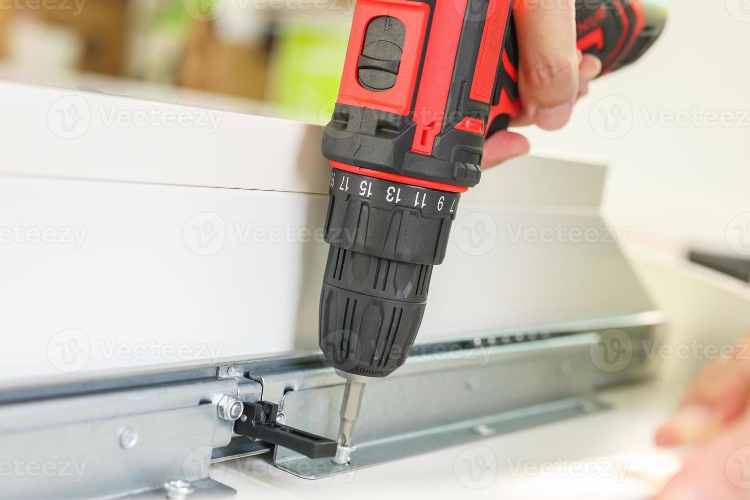 man assembling white table furniture at home using cordless screwdriver photo