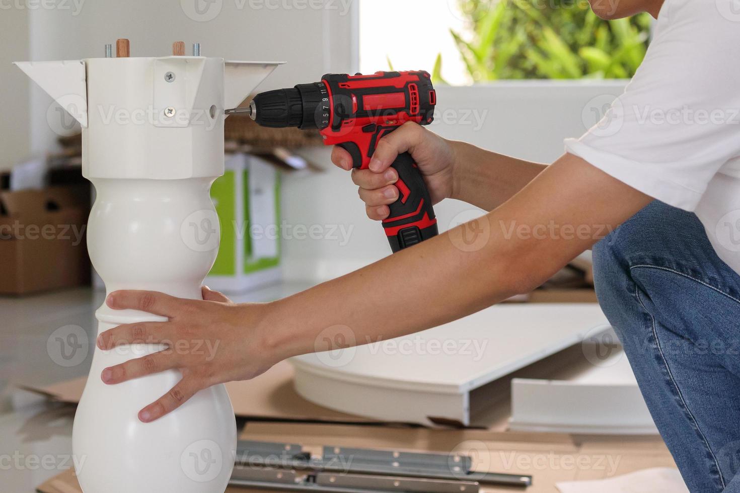 man assembling white table furniture at home using cordless screwdriver photo