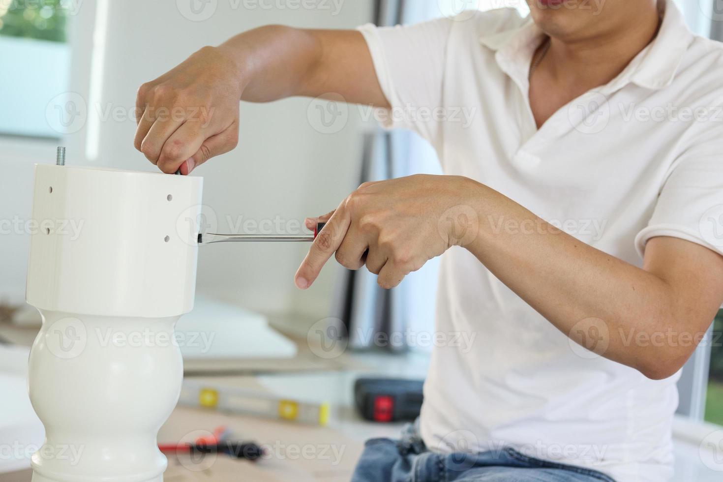 Asian man assembling white table furniture at home photo