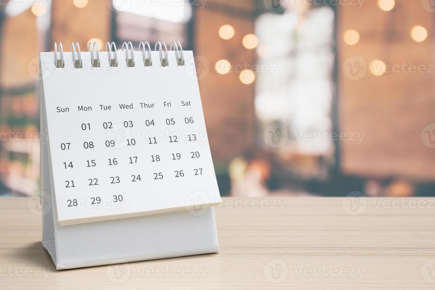 calendario de escritorio de papel blanco sobre una mesa de madera con una cita de fondo borrosa y concepto de reunión de negocios foto