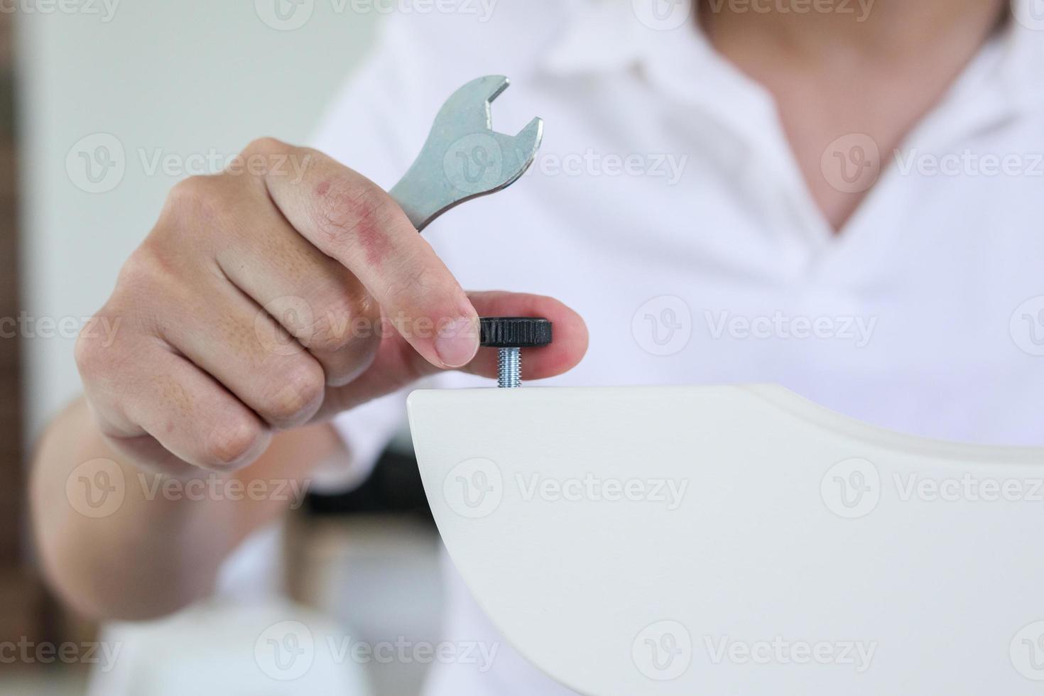Asian man assembling furniture at home with adjustable table leg photo