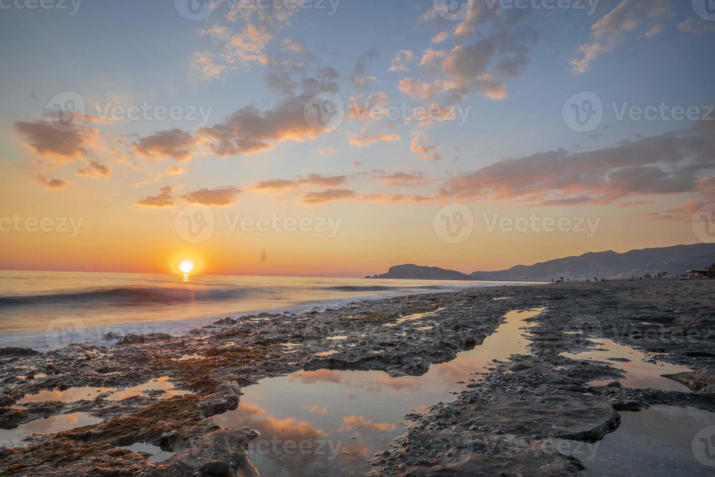 hermosa toma de una larga puesta de sol cálidos tonos de naranja, amarillo, rosa, azul y morado. agua suave y reflejo foto