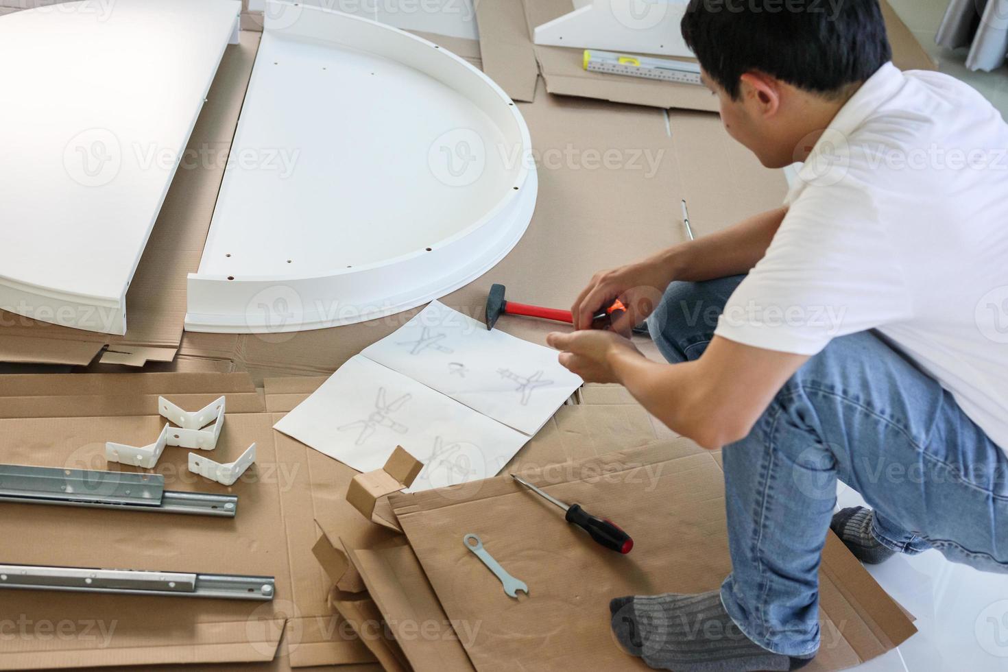 Asian man assembling white table furniture at home photo