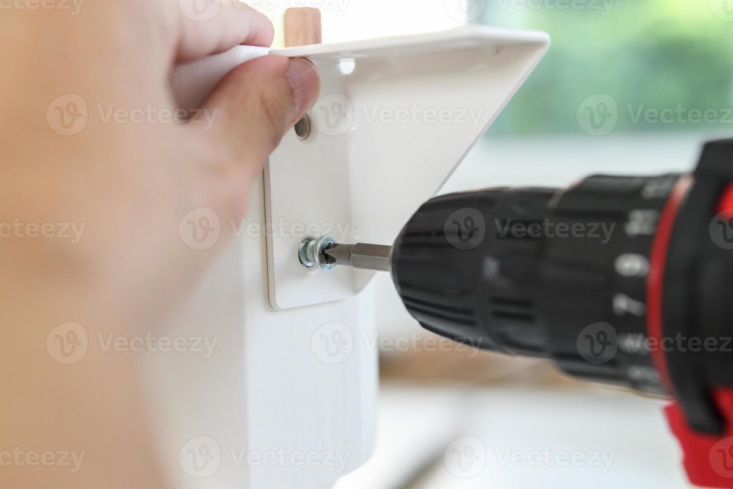 man assembling white table furniture at home using cordless screwdriver photo