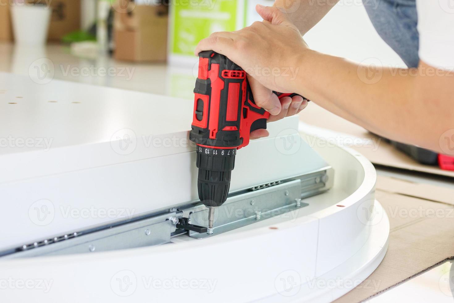 man assembling white table furniture at home using cordless screwdriver photo