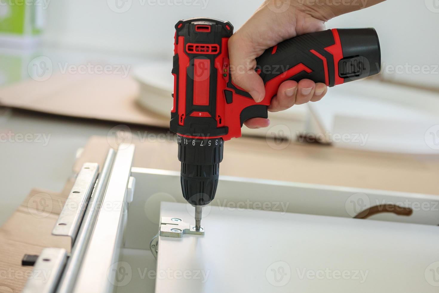man assembling white table furniture at home using cordless screwdriver photo