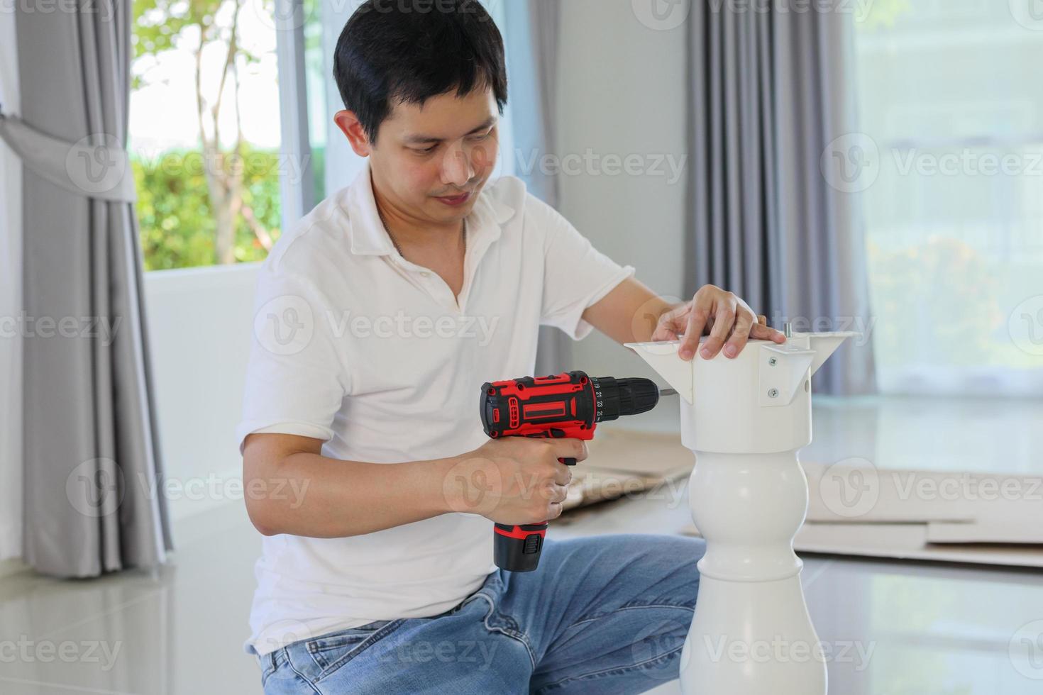Asian man assembling white table furniture at home using cordless screwdriver photo