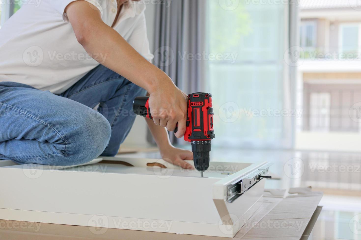 man assembling white table furniture at home using cordless screwdriver photo