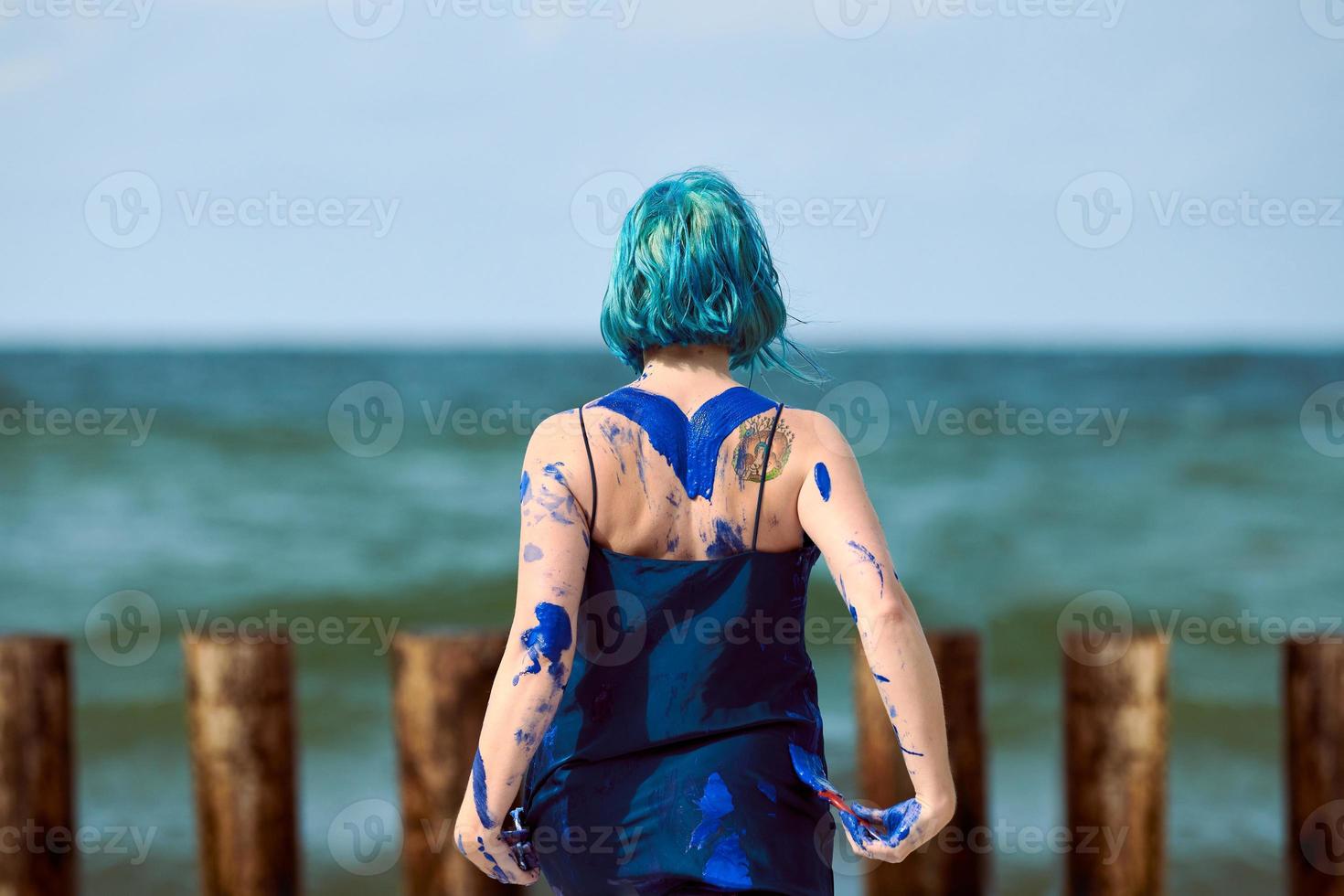 artista artística de cabello azul con vestido manchado con pinturas de gouache azul en su cuerpo foto