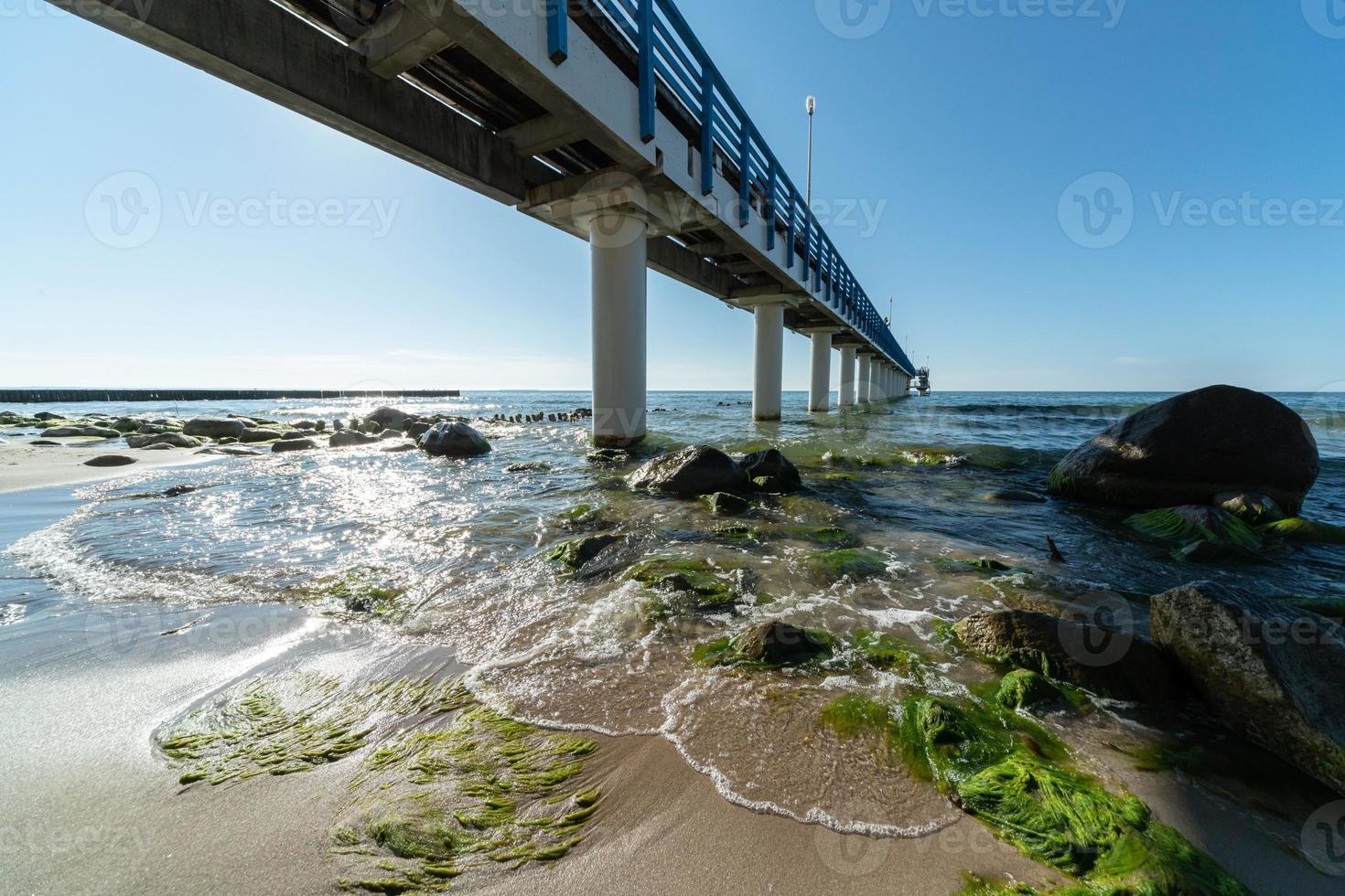 Muelle turístico en zona de playa. hermosa costa a la luz del sol. olas de surf con espuma de mar y algas. paisaje marino de día. foto