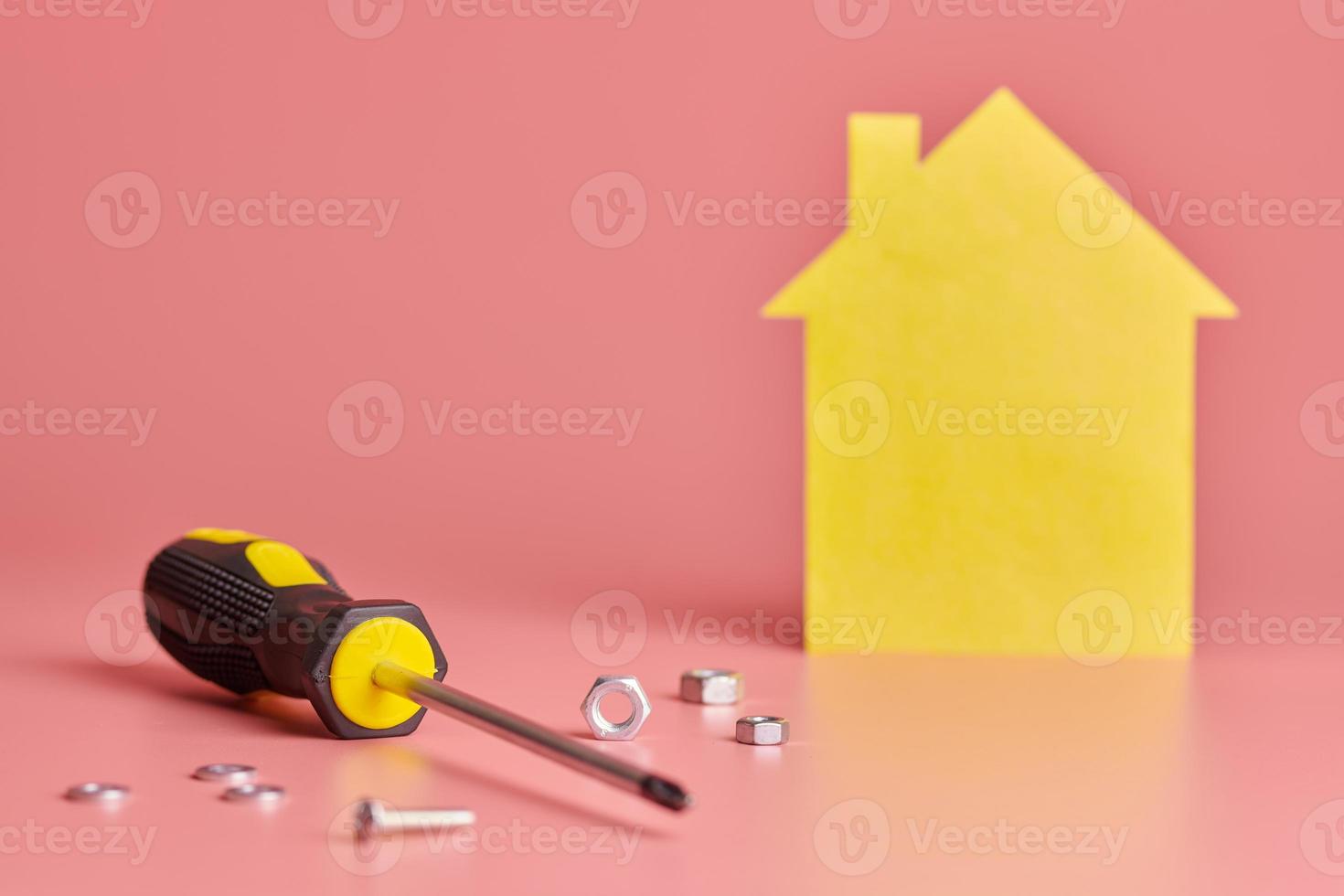 Home repair and redecorated concept. House renovation. Screws and yellow house shaped figure on pink background. photo