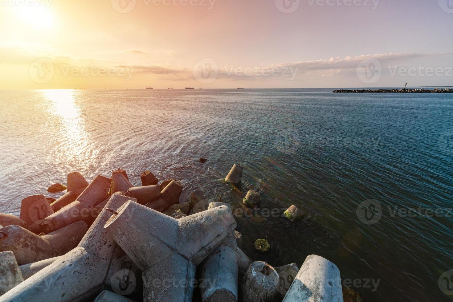 Beautiful sunset seascape. Travel dreams and motivation. Breakwaters tetrapods on shore of pier. Cargo ships on the horizon. photo