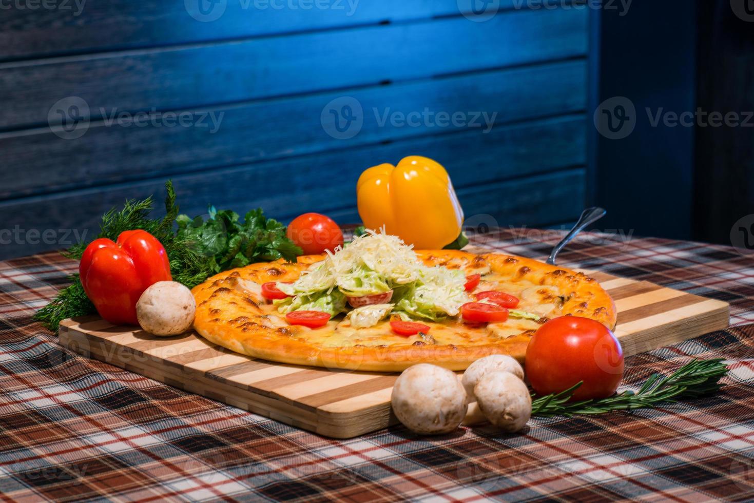 A closeup of table for lunch, pizza, vegetables, yellow and red peppers, mushrooms on wooden board photo