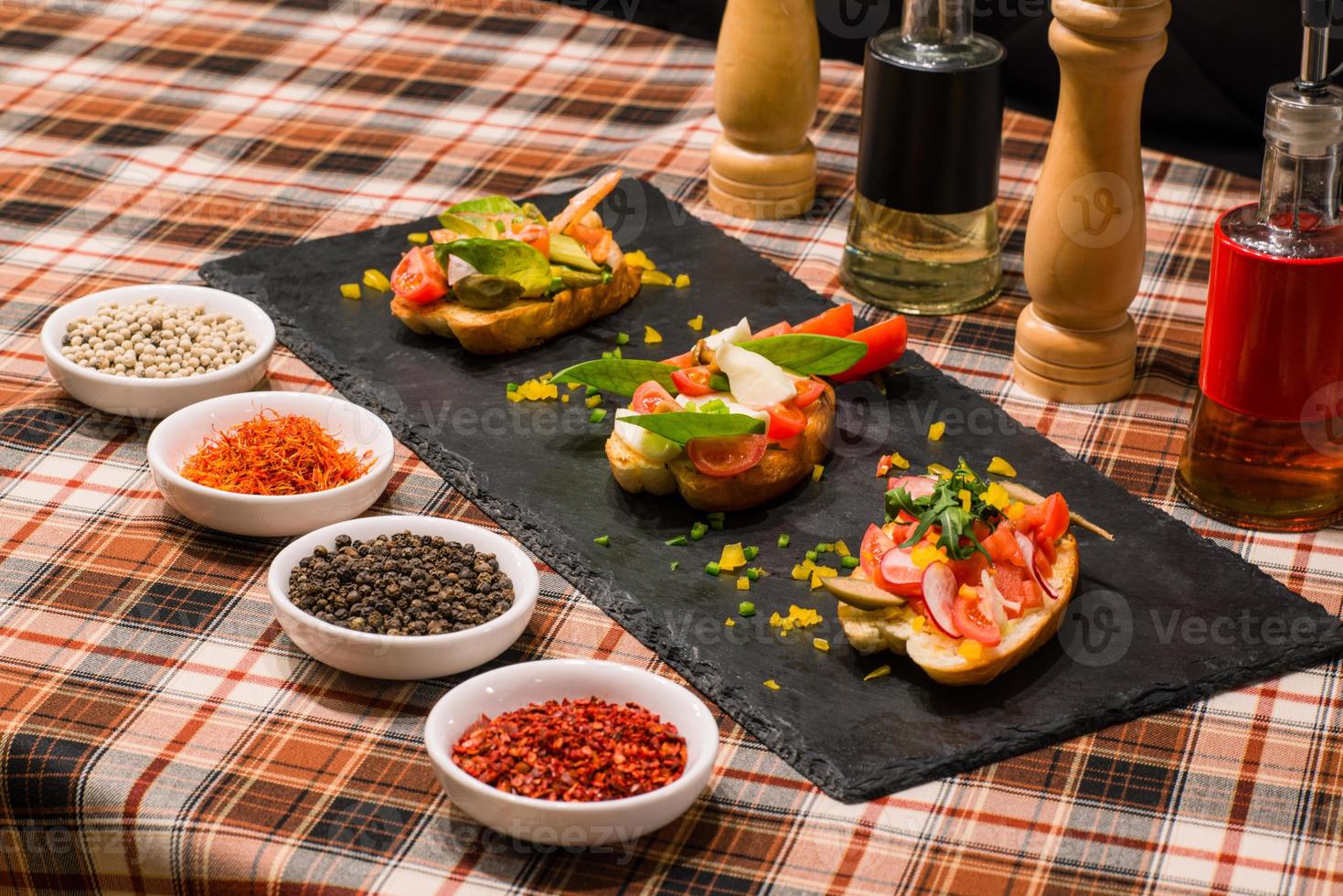 A closeup of serving table with tasty sandwiches or bruschetta with vegetables and spices on black board photo
