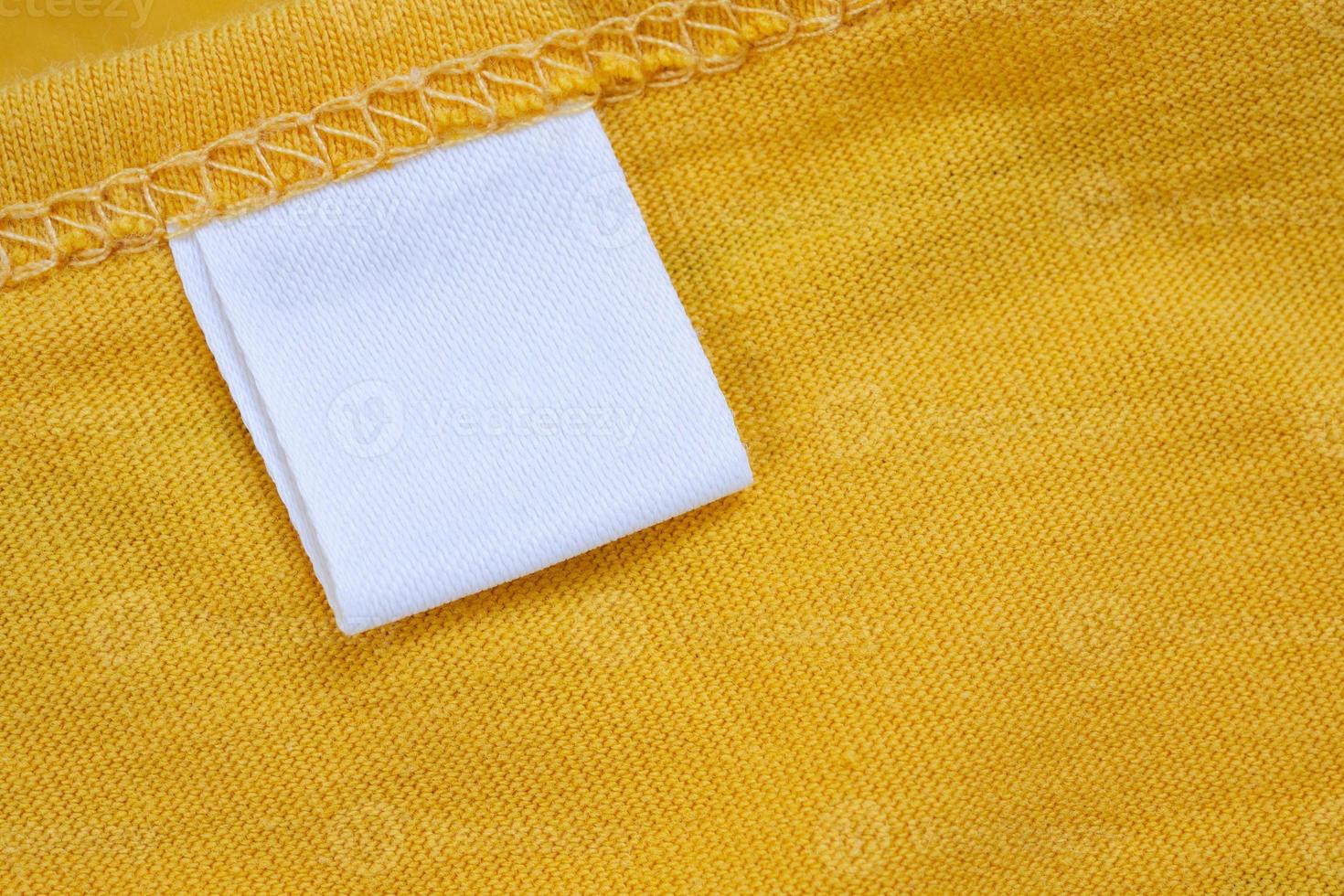 White blank clothing tag label on new yellow shirt background photo