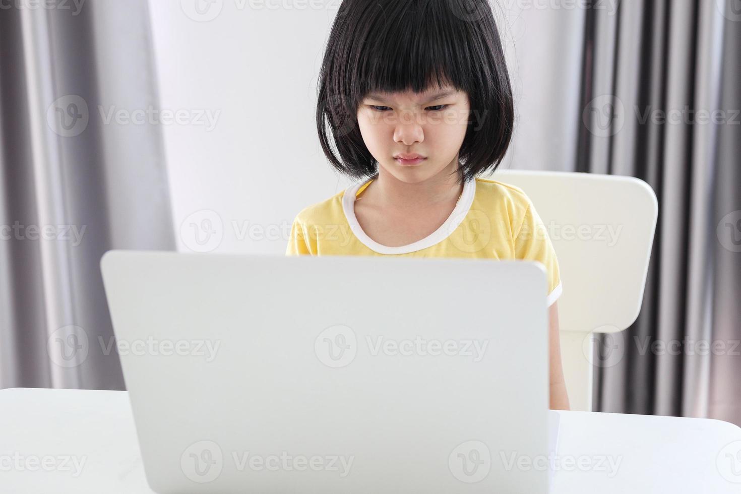 little asian girl student study online using laptop computer at home photo