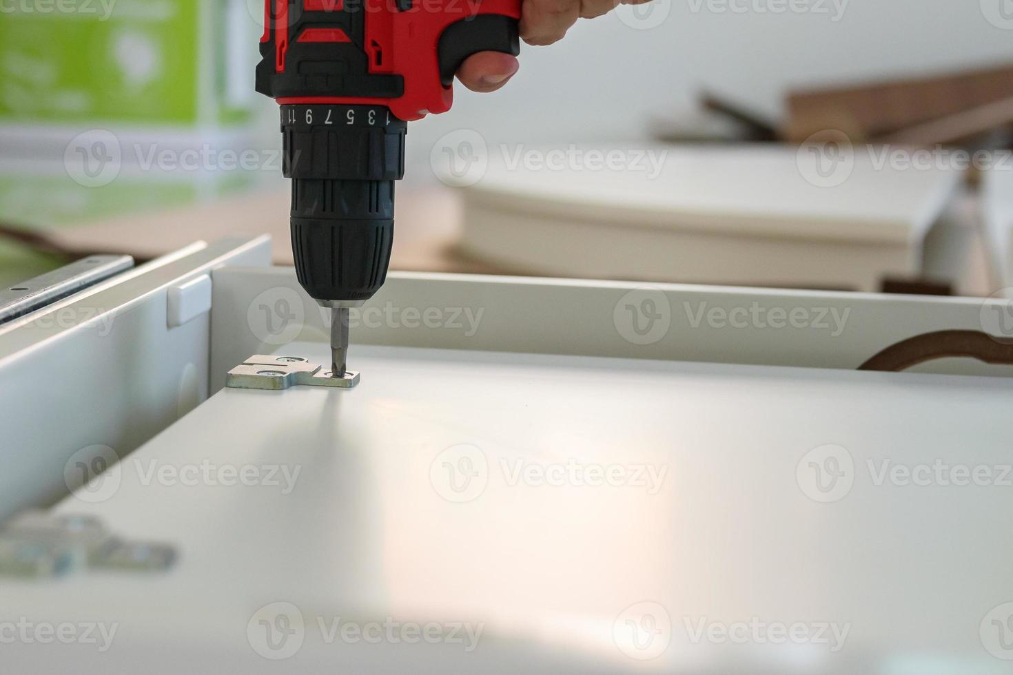 man assembling white table furniture at home using cordless screwdriver photo