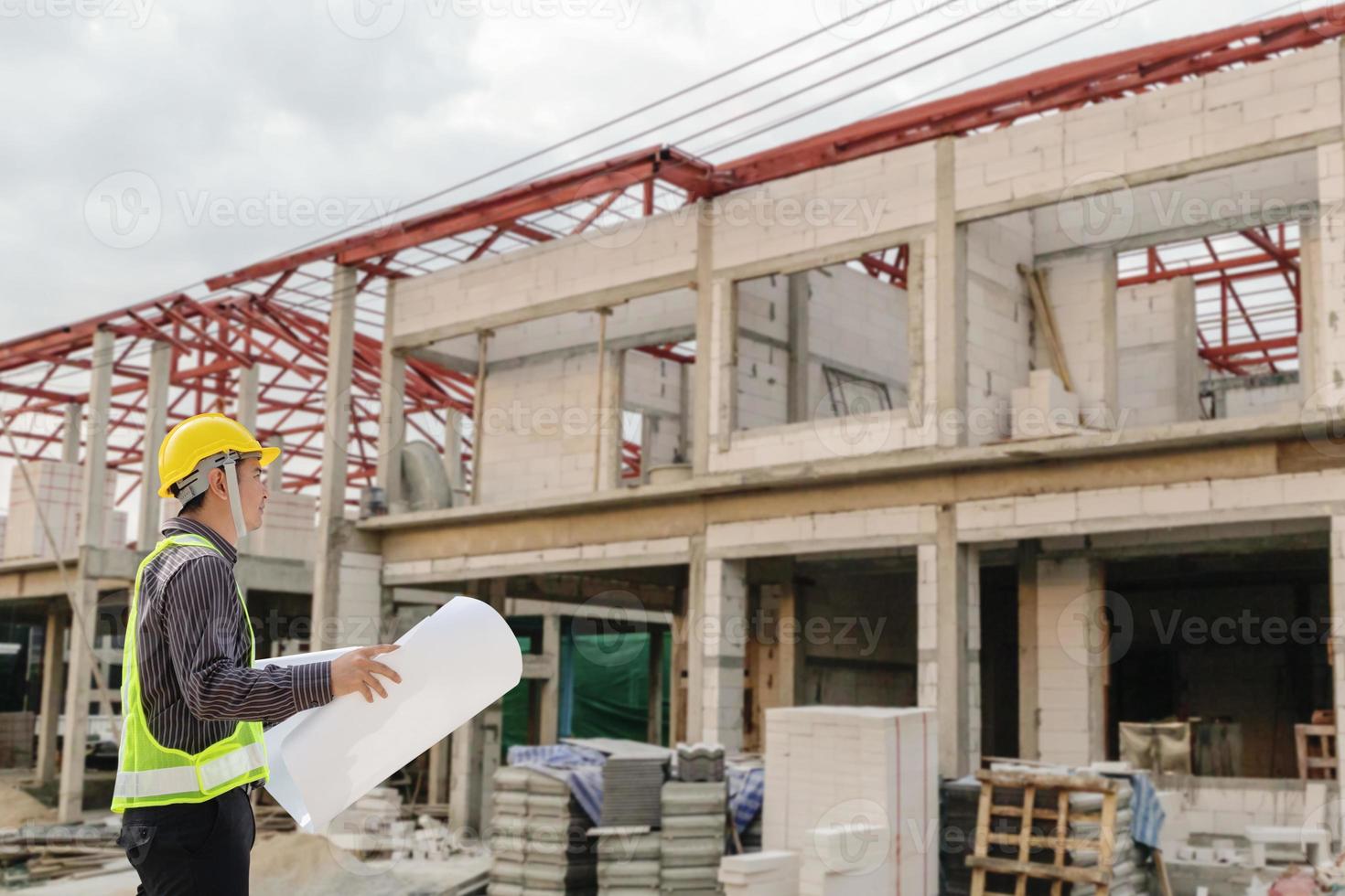 young professional engineer in protective helmet and blueprints paper at the house building construction site photo