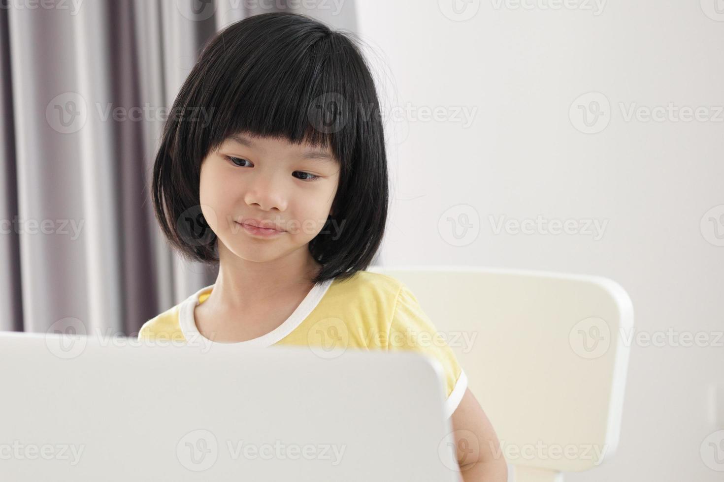 little asian girl student study online using laptop computer at home photo